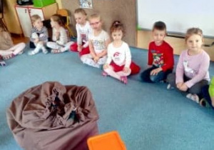 Dzieci siedzą na dywanie i czekają na prezenty z worka Mikołaja
